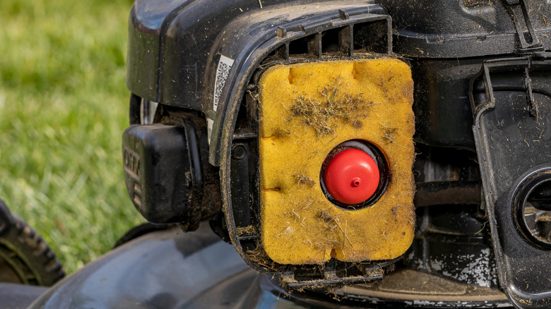 A dirty yellow and red foam air filter inside a lawn mower motor.