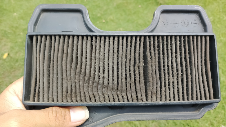 A person holds a dirty paper lawn mower air filter up to the camera lens.