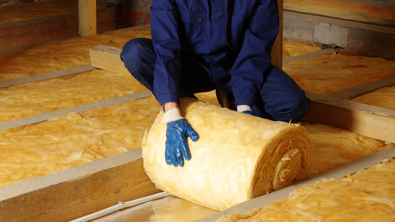 Person unrolling insulation in attic