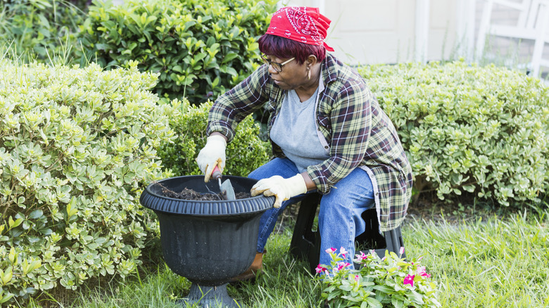 Woman planting flowers in large planter pot.