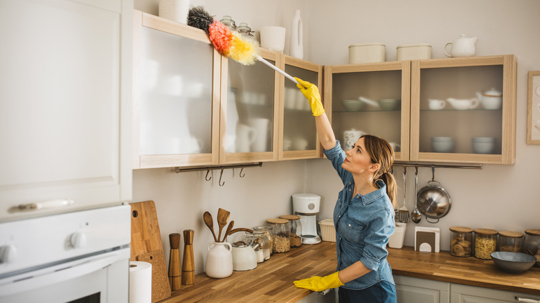 Woman dusting the top of kitchen cabinets