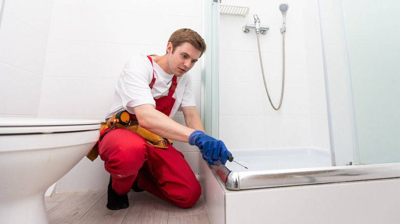 person in red overalls repairing shower tray