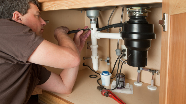 Man working on a garbage disposal under a sink