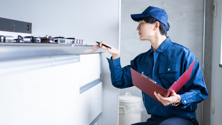 A person inspecting a gas stove wearing a blue uniform