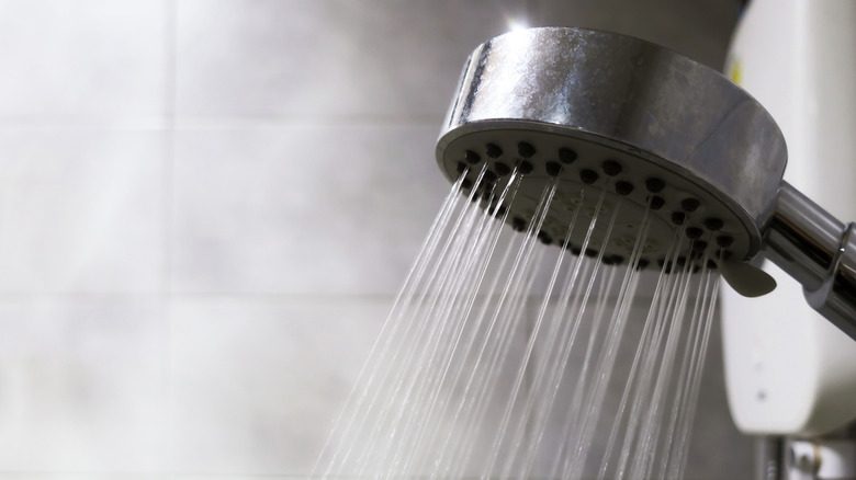 A close up of a shower head with hot water coming out and steam in the background