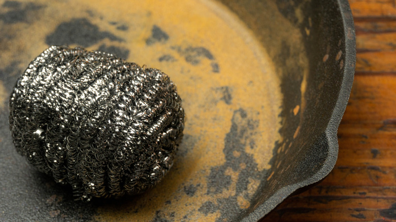 A steel wool scrubber on a rusty cast iron pan.