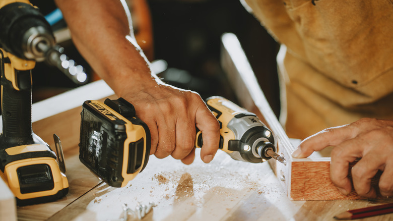 A man uses a DeWalt drill to insert a screw that is connecting two pieces of wood at a right angle.