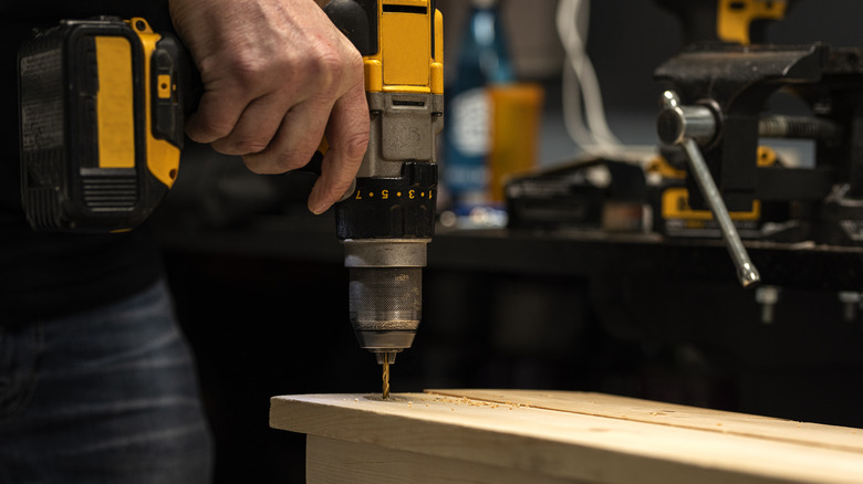 A person uses a drill on a piece of wood.
