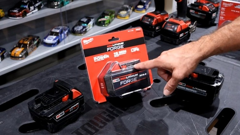 Hand pointing to Milwaukee M18 lithium forge battery in packaging next to chargers