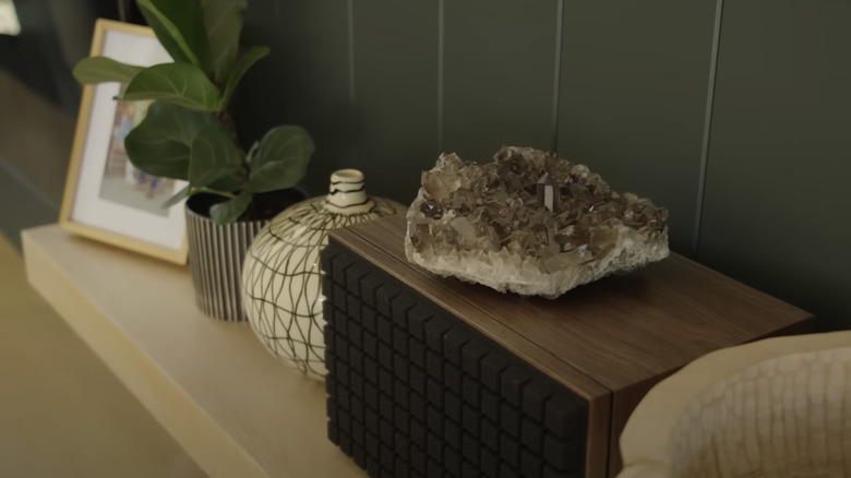 A large smoky quartz crystal sits on a wooden speaker next to tribal vases