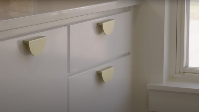 Gold half-moon shaped pulls are installed on white drawers