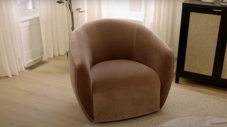 A sable velvet armchair sits next to a black and rattan sideboard