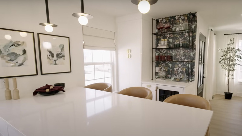 Three leather stools and a wallpaper backed bar are behind a large white kitchen island