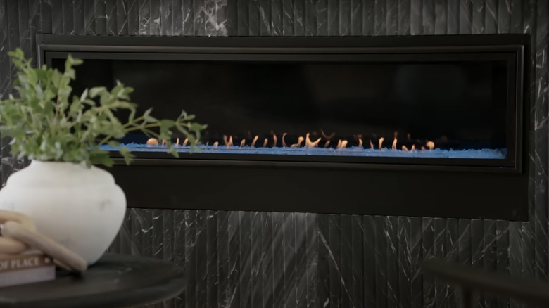 A matte white vase with greenery sits in front of a linear gas fireplace
