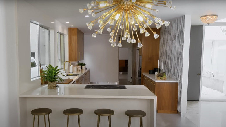 A gold Sputnik chandelier hangs over an infinity edge kitchen island and four bronze stools