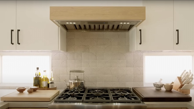 White cabinets with black handles flank a stainless steel stove and ceramic tile backsplash