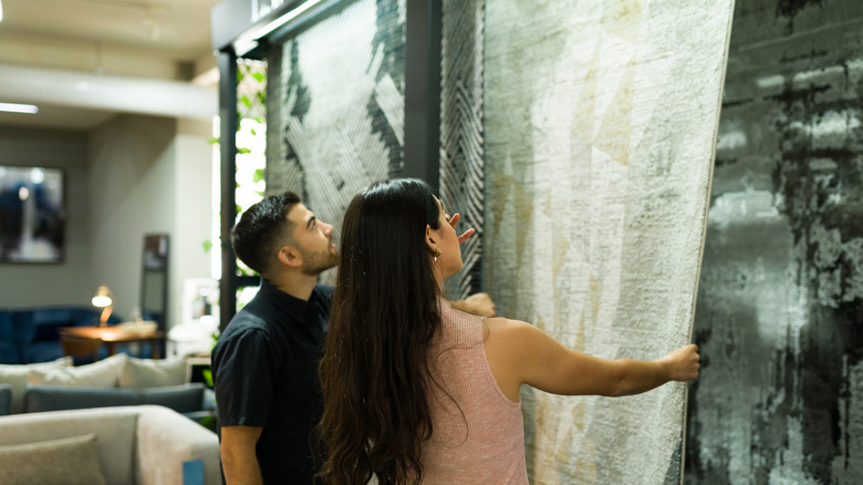 a couple looks at hanging rugs in a store