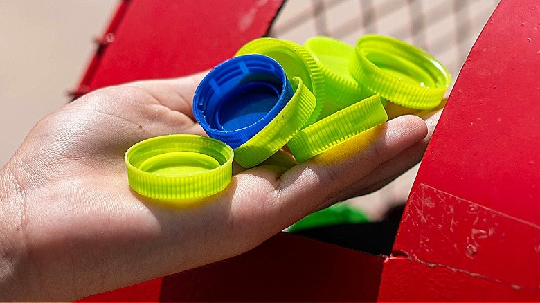 Close-up of a hand holding several green bottle caps and one blue one