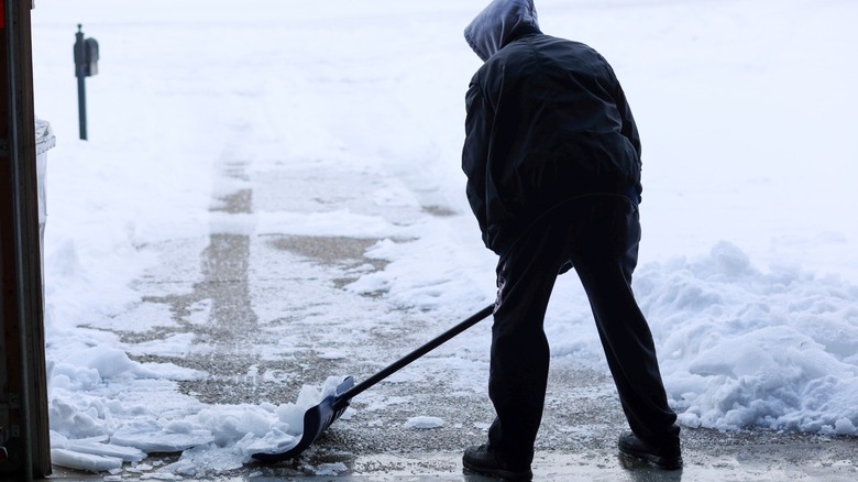 Person shoveling snow-covered icy driveway
