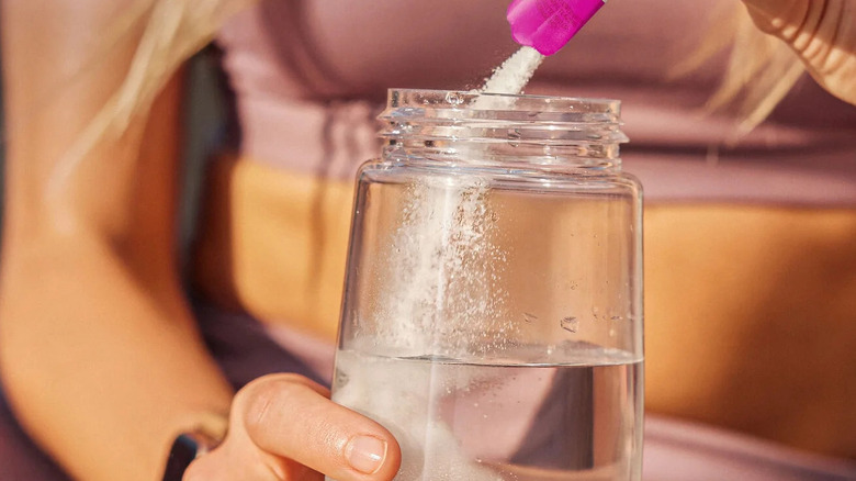 grape flavor drink powder being poured into glass jar of water