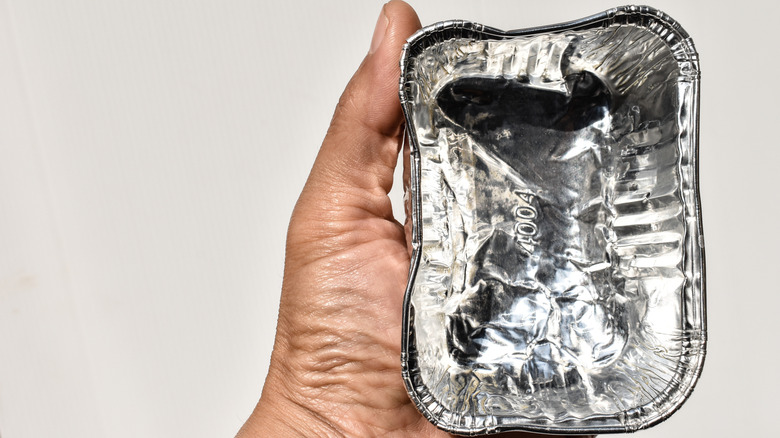 A hand holding a small disposable aluminum foil dish
