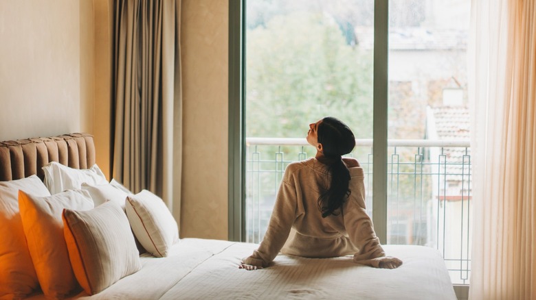 woman sitting on bed in front of window with curtains pulled back