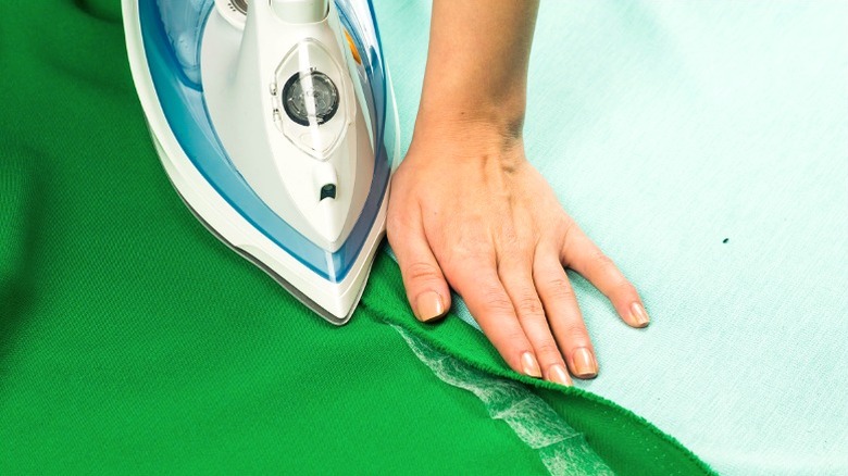 person ironing hem on green tablecloth fabric with fabric fuse tape