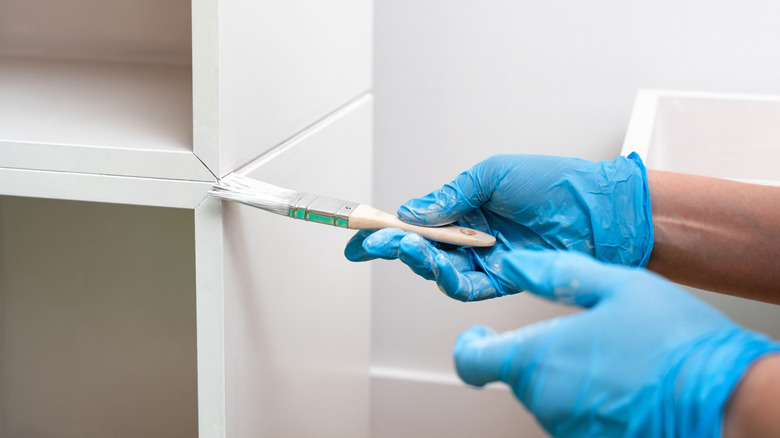 Hands in blue gloves painting a white cabinet