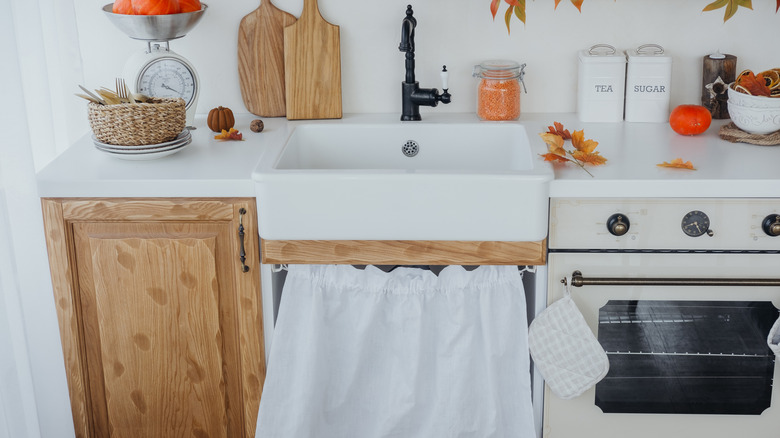 A small kitchen with a farmhouse sink and skirt.