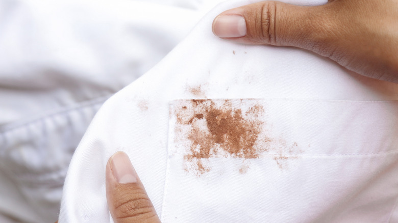 Hands holding a white shirt with a visible brown stain on it