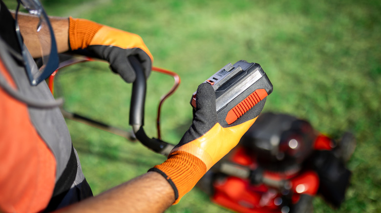 An individual holding a battery of a electric mower