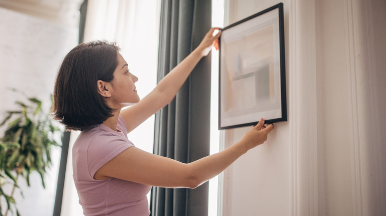 Woman hanging a simple black-framed wall art on the wall.