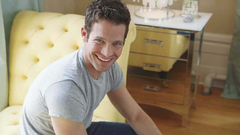 Nate Berkus sitting on a yellow upholstered chair and smiling at the camera