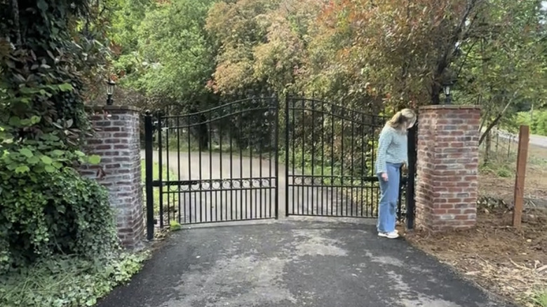 A woman standing in front of a large driveway gate.