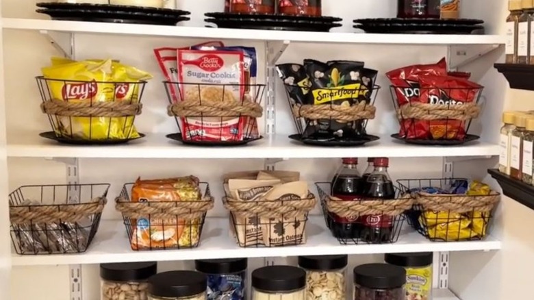 Snacks are stored in Dollar Tree wire baskets embellished with decorative rope on a kitchen pantry shelf.
