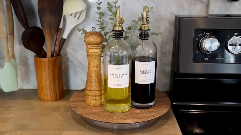A wooden lazy Susan rests beside the stove with bottles of olive oil and balsamic vinegar on top along with a pepper grinder.