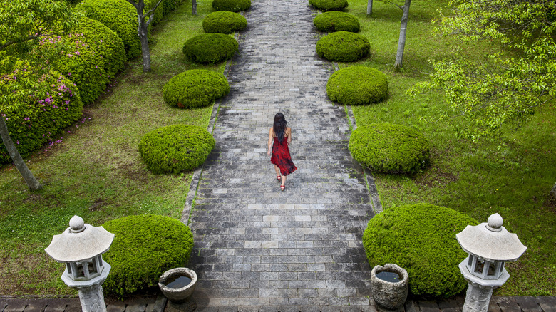 Woman walking on stone path lined by round hedges