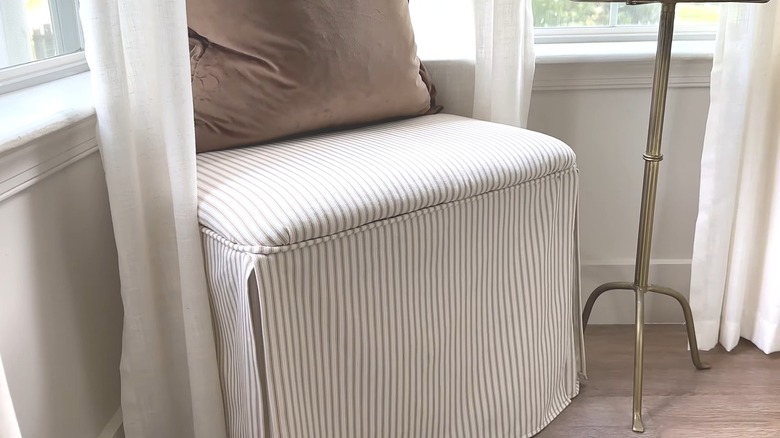 Thrifted ottoman reupholstered in a striped fabric sitting in the corner of a living room near windows