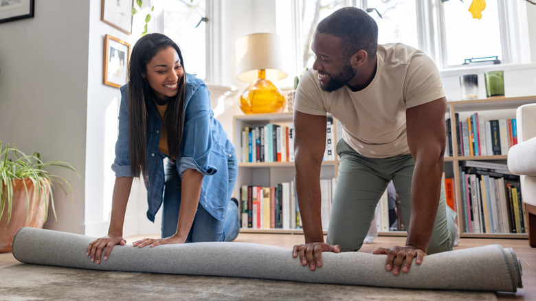 Couple unrolling an area rug together over a wood floor in the living room