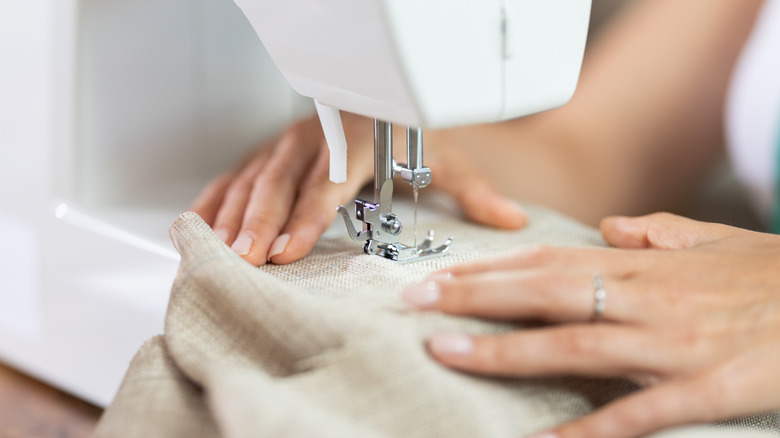 Person guiding beige fabric through a sewing machine