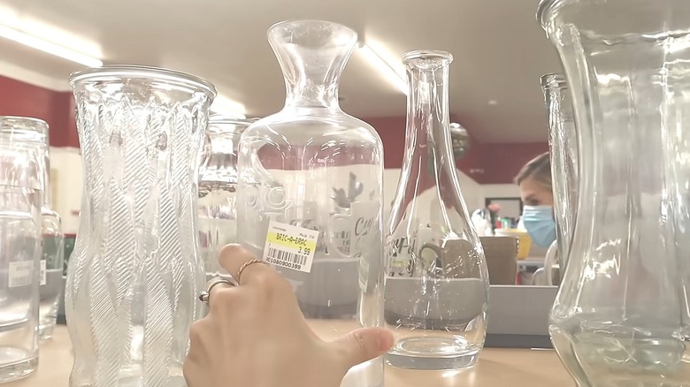 Person reaching for a glass vase on a thrift store shelf