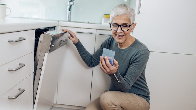 woman on smartphone opening dishwasher