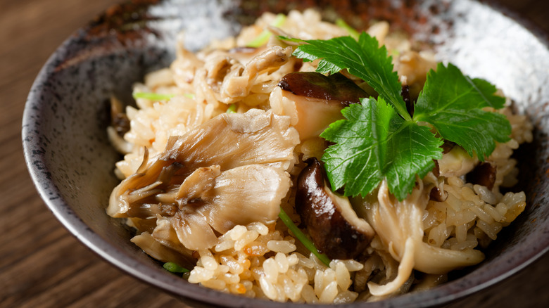 Bowl of glazed rice and gourmet mushrooms with a parsley garnish on a wooden coutnertop