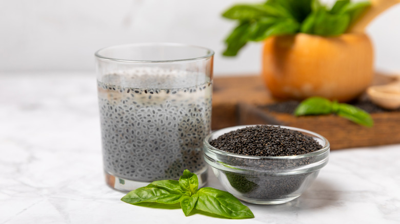A sprig of basil next to a bowl of basil seeds