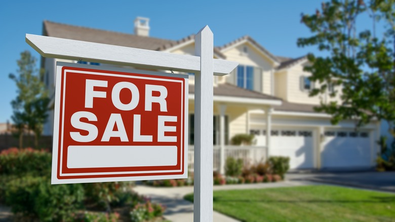 A 'For Sale' sign in front of a large house