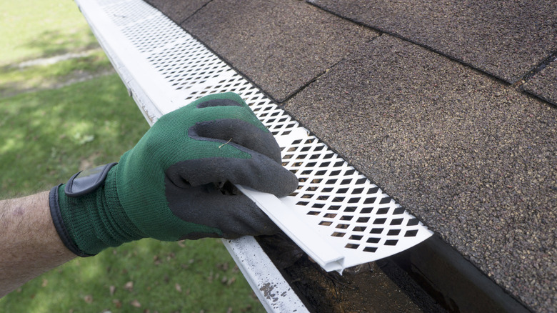 A set of grates is being installed in rooftop gutters by someone in a green-gloved hand.