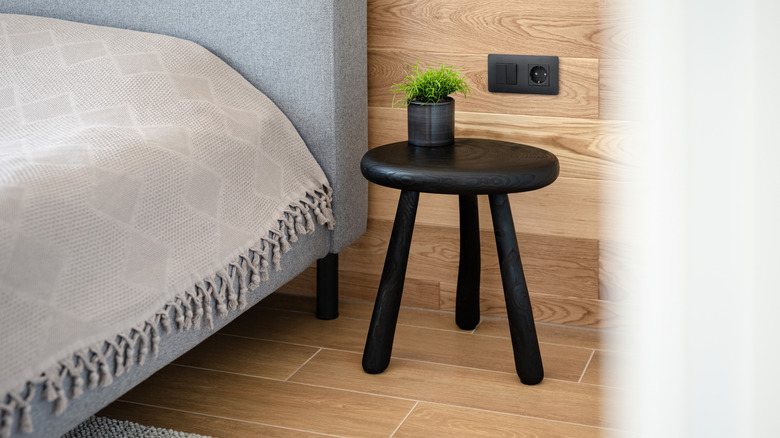 A Yakisugi bedside table supports a potted plant in a wooded room near a bed