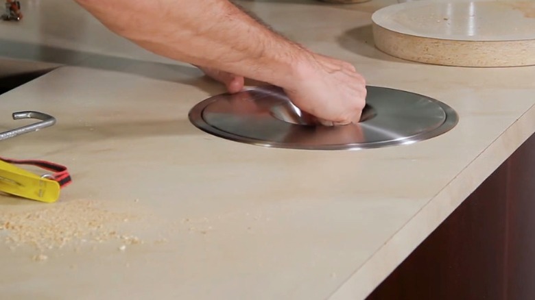 A person installs a round trash chute in kitchen countertop