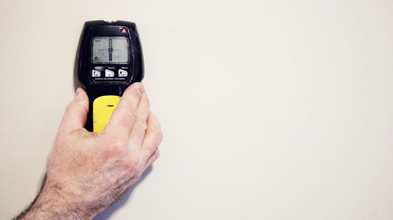 Person using a stud finder on bare drywall