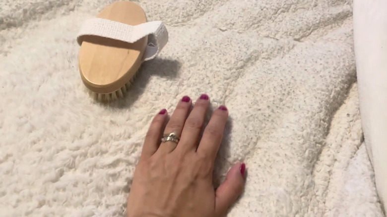 Woman's hand and boar bristle brush on top of a white sherpa blanket